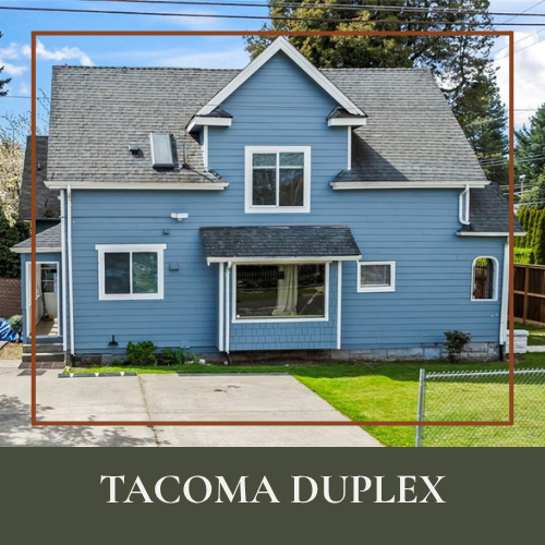 A blue duplex house with white trim, a steep gray roof, and a small covered front porch, located in a residential neighborhood.