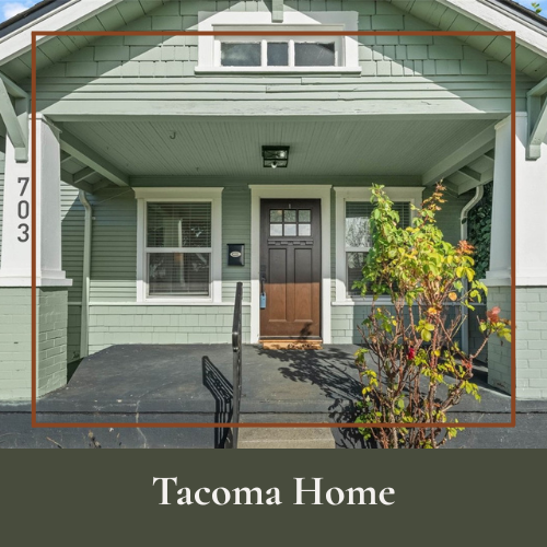 Front entrance of a green Tacoma home with a black door, two windows, a small porch, and a shrubbery on the right side.