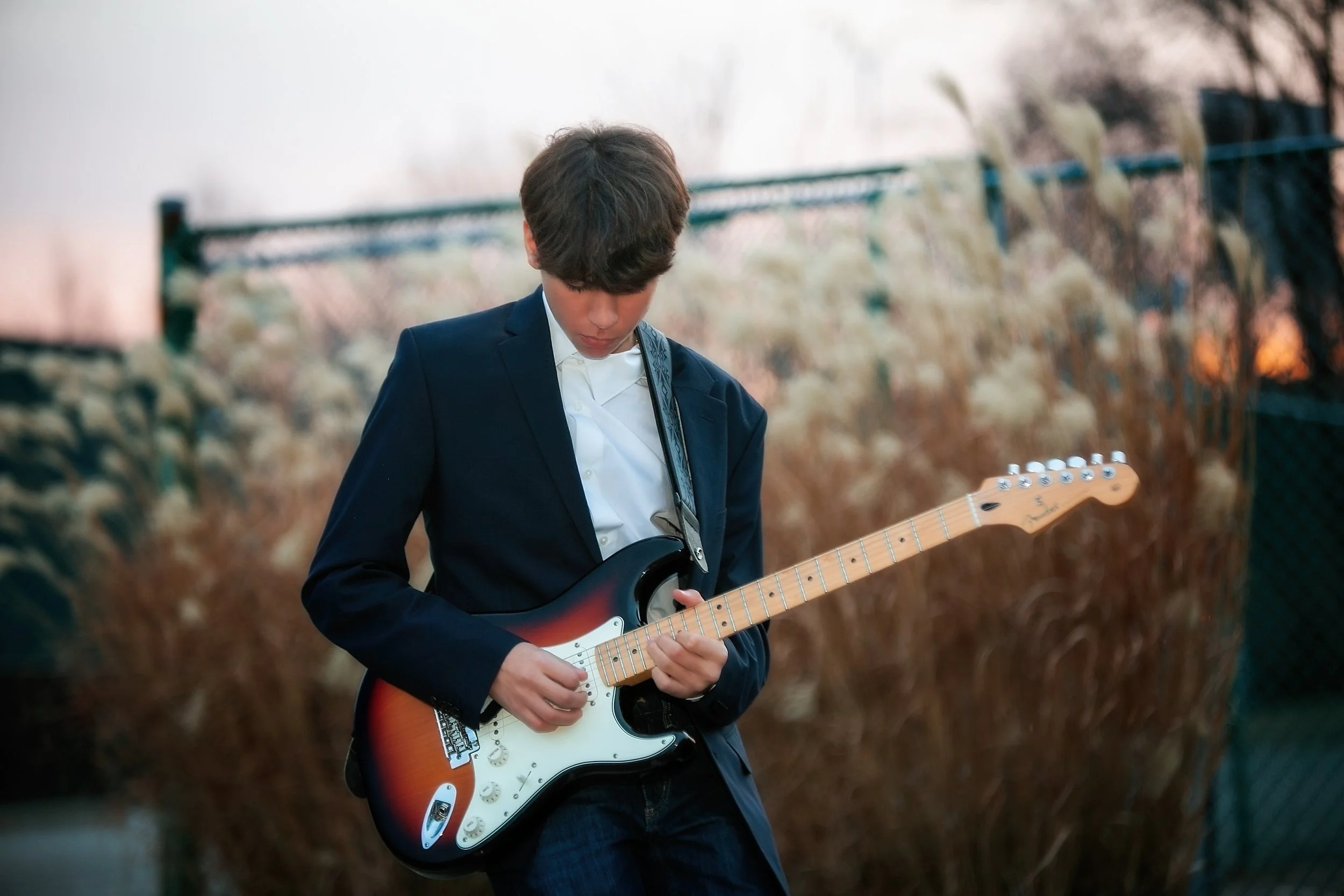 Young man in a suit playing an electric guitar outdoors during sunset.