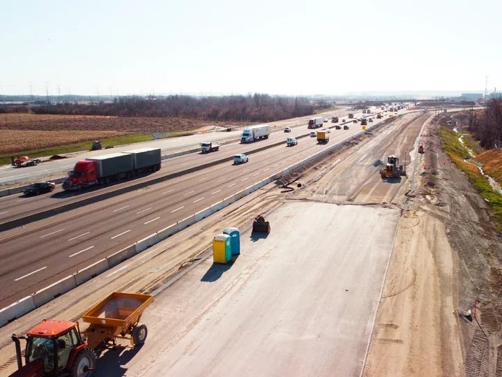 Construction work on a highway with trucks, construction vehicles, and porta potties.