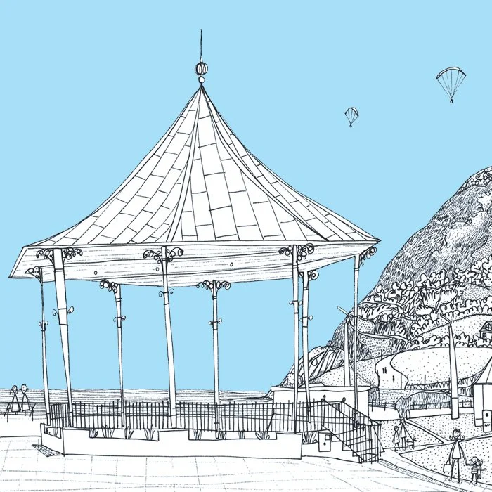 Black and white line drawing of the bandstand at Bray Promenade, with a mountainous landscape and people in the background, and parasails in the sky.