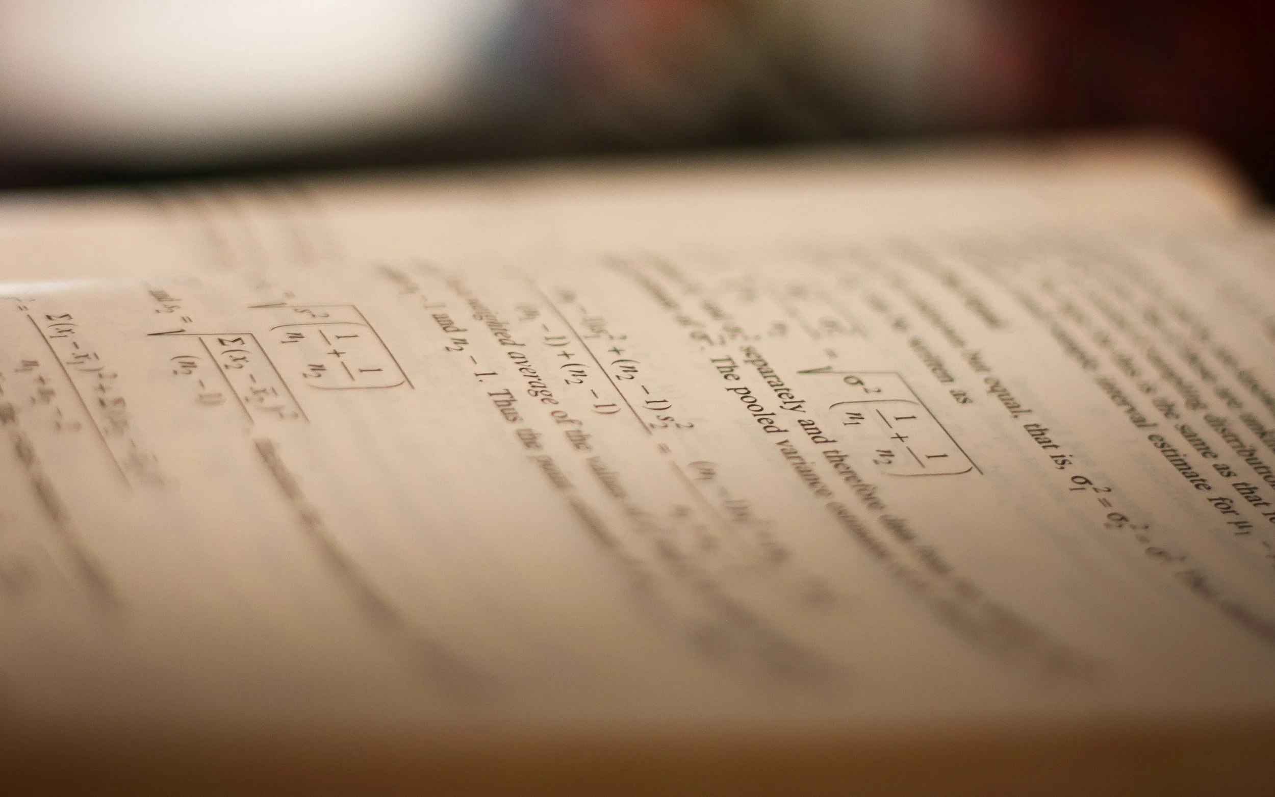 Close-up of a page with handwritten mathematical problems and notes in black ink, with a blurred background.