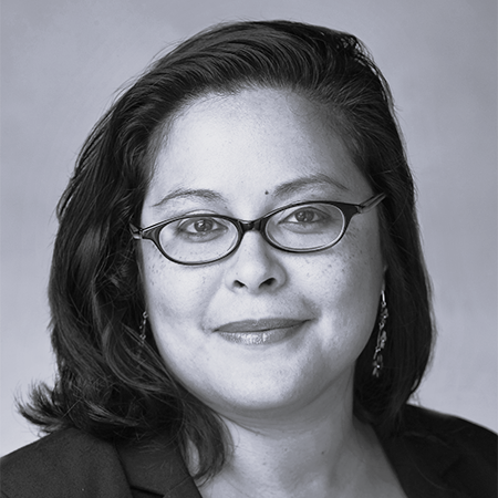 Black and white portrait of a woman with glasses, shoulder-length hair, earrings, and a confident smile.