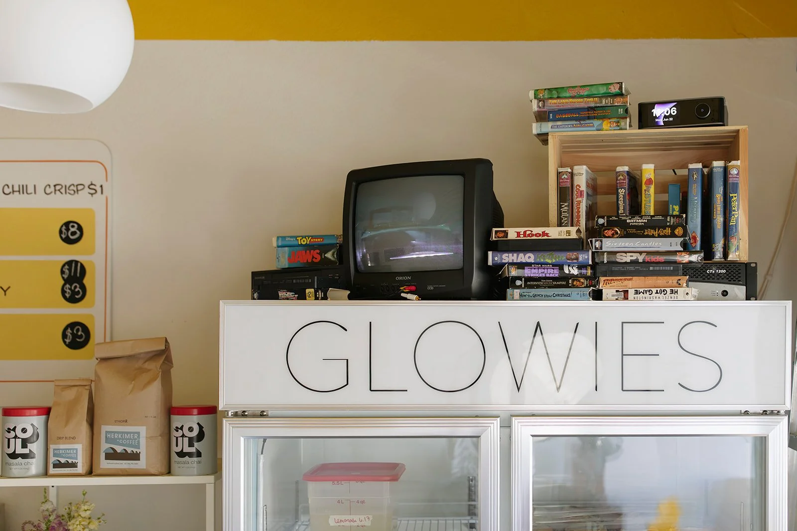 Display of DVDs, a vintage TV, a wooden shelf, and a sign with the word 'GLOWS' in a store.