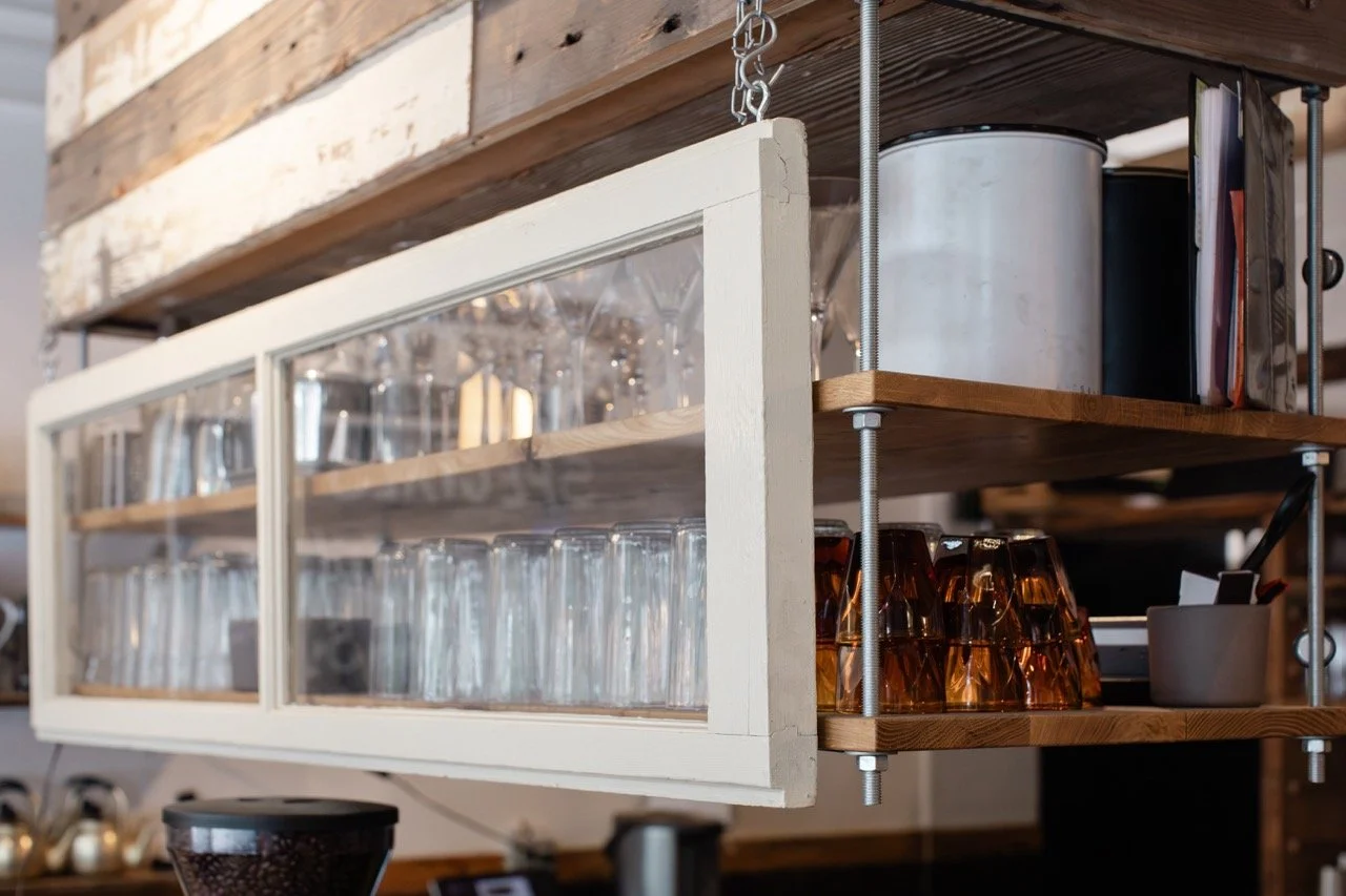 Wood and glass shelving unit with glasses and mugs in a cafe or kitchen setting.
