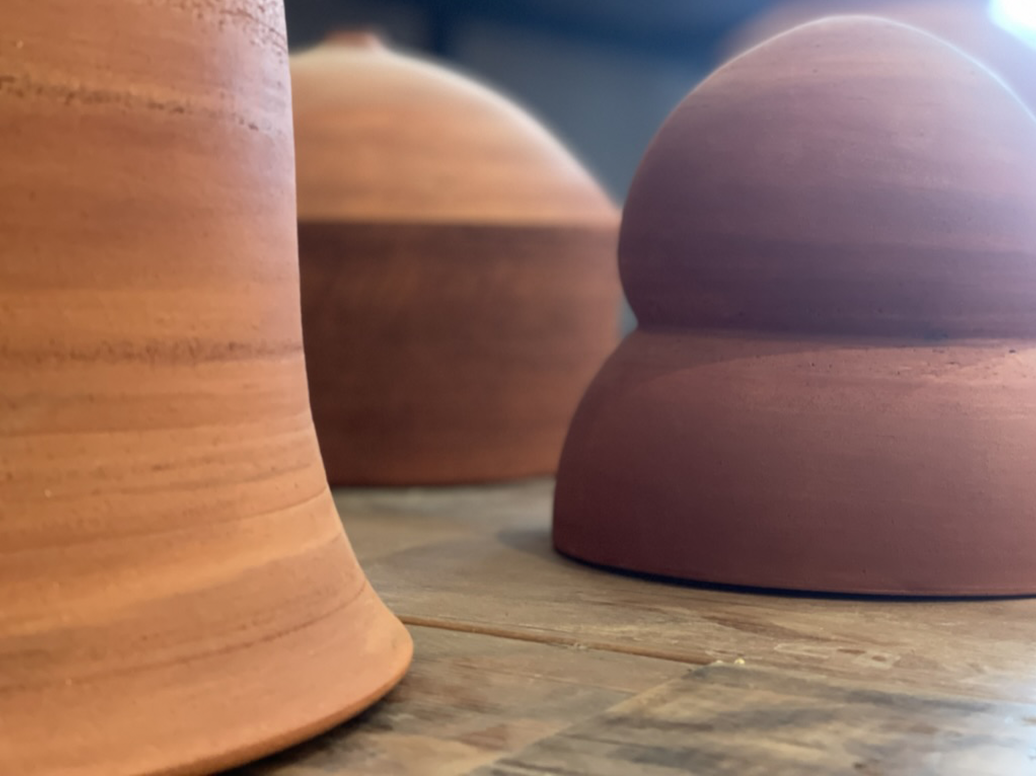 Close-up of several terracotta pottery vases with a smooth, rounded shape, arranged on a wooden surface.