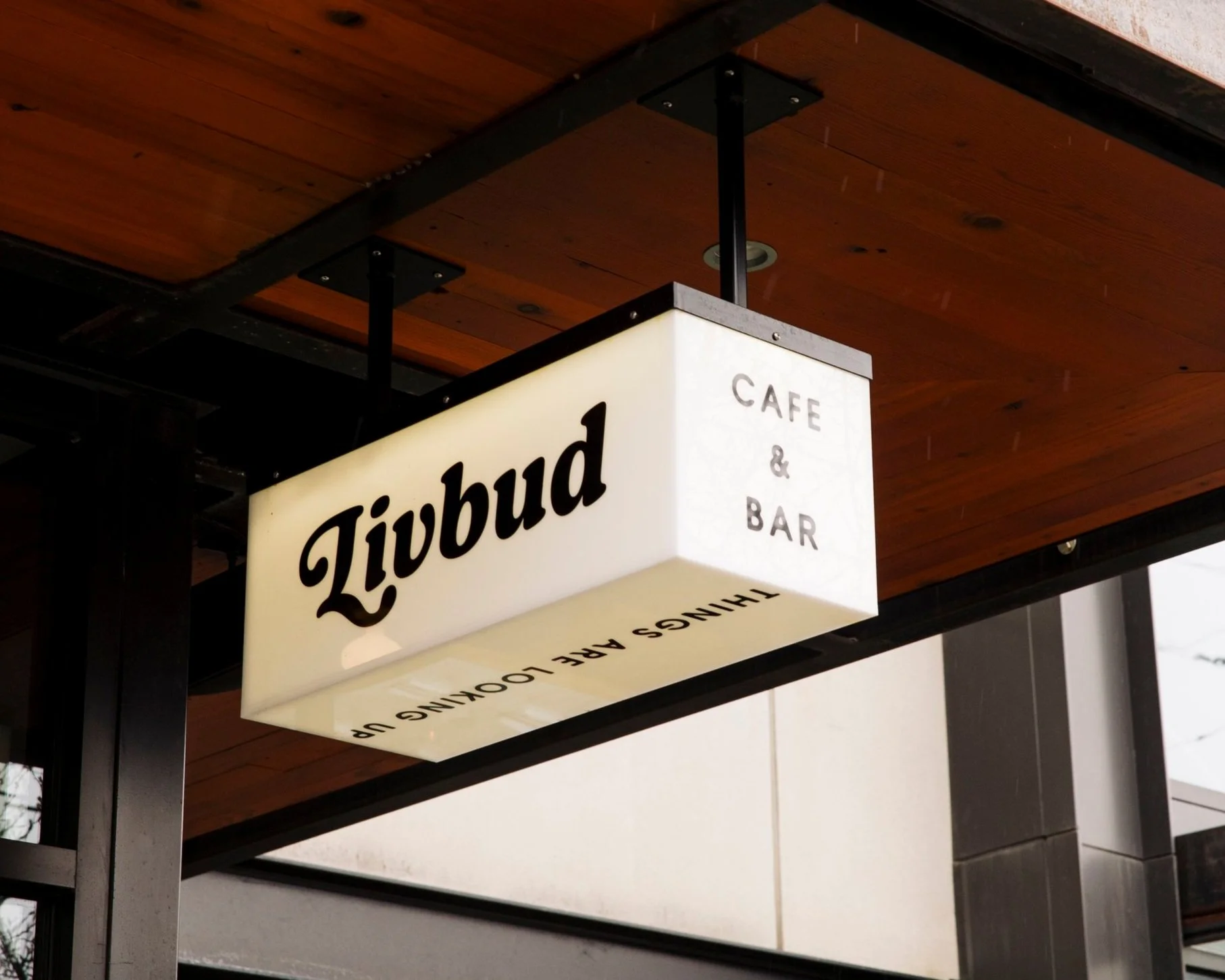 Sign for Livbudd Cafe and Bar hanging from a ceiling with a wooden background.