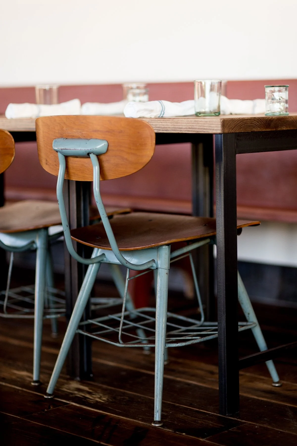 Wooden chairs around a wooden table set with glasses and cloth napkins in a restaurant.