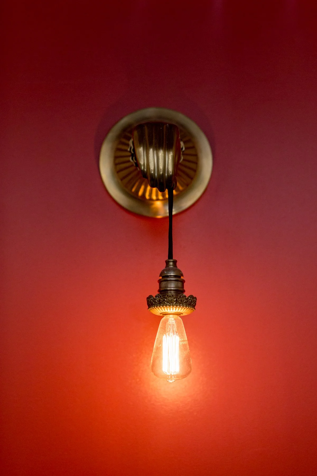Close-up of an industrial-style pendant light with a vintage filament bulb hanging from a ceiling with a red wall background.