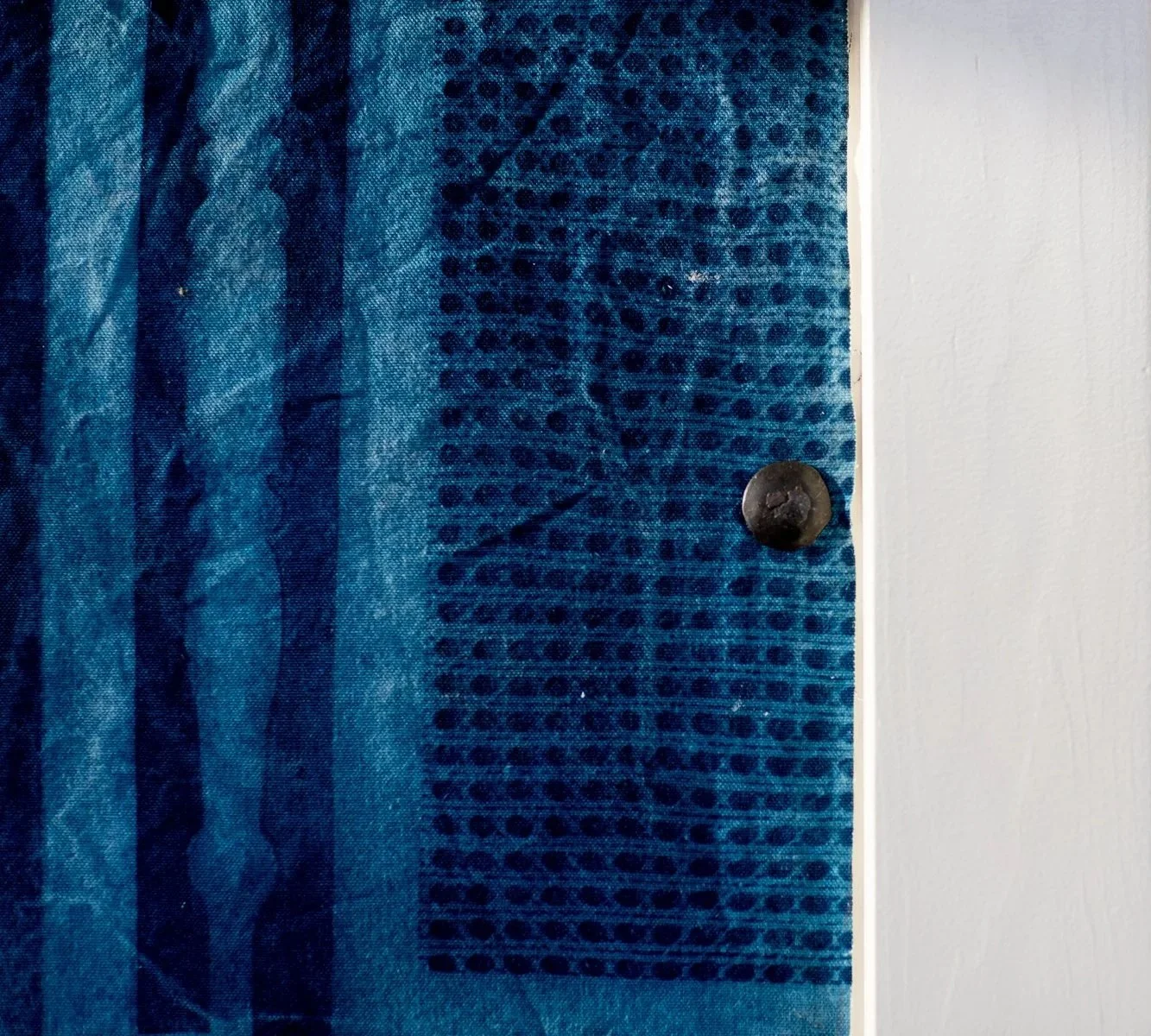 Close-up view of a blue textured surface on the left and a white wall on the right, with a dark round screw or bolt partially embedded in the surface on the right side.