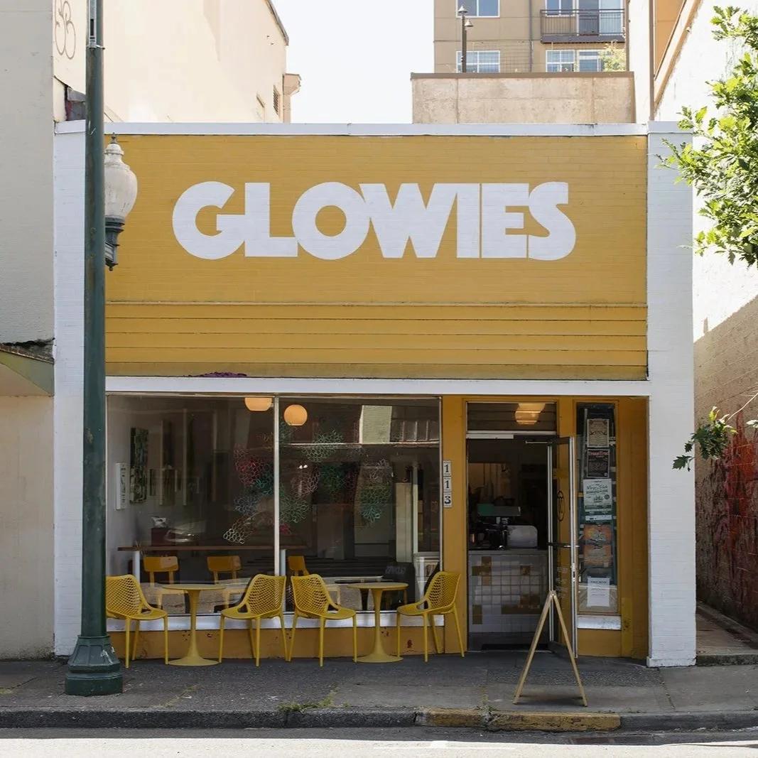 Front of a small café with a yellow exterior and a large sign that says GLOWIES. There are yellow chairs outside, and the interior is visible through large windows.