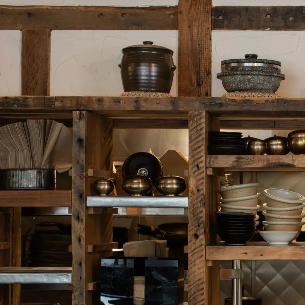 Wooden kitchen shelving with ceramic and metal bowls, pots, and plates arranged on the shelves.