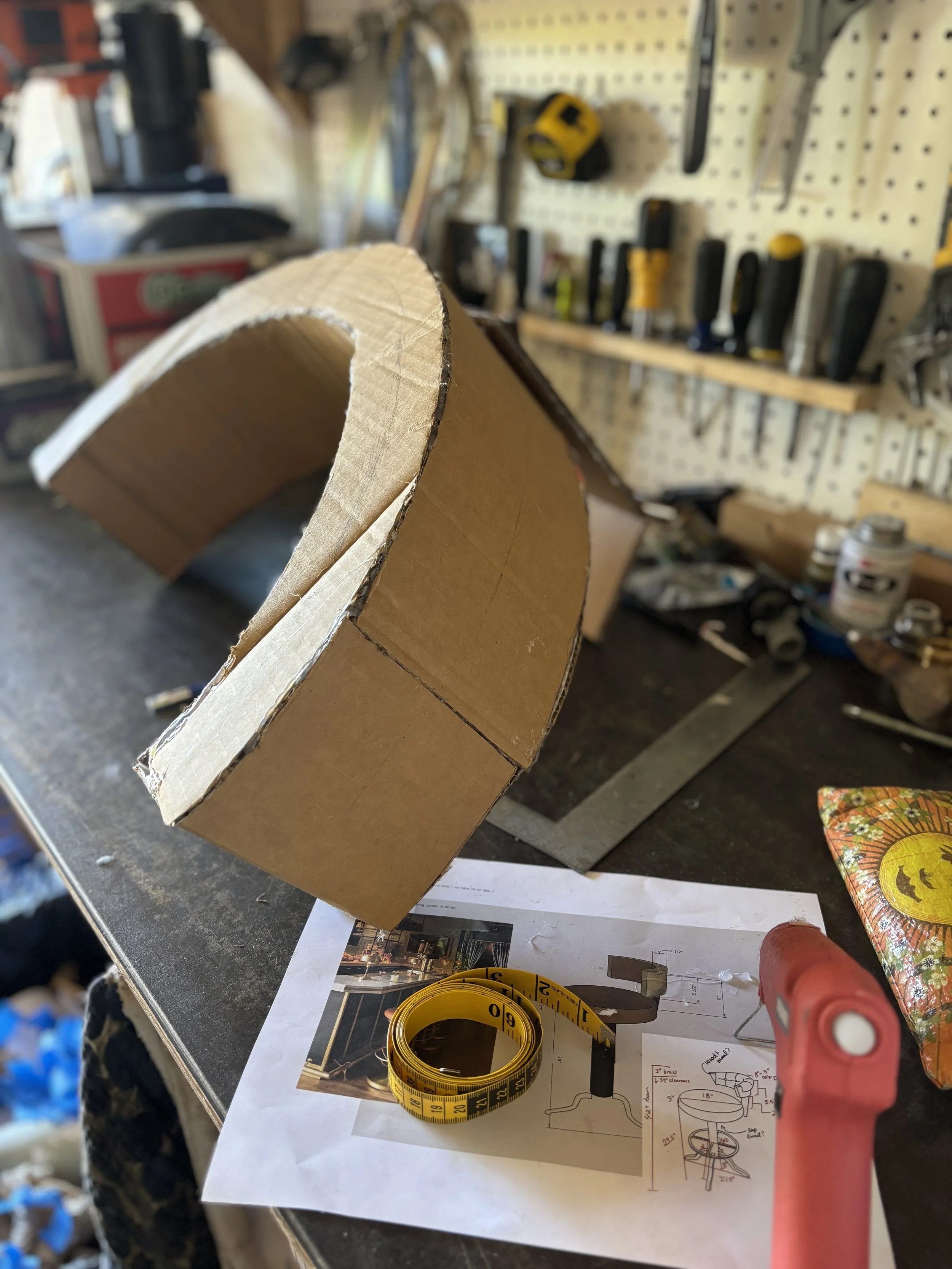 A cluttered workbench in a woodworking workshop with woodworking tools, measuring tape, and project plans scattered on the surface.