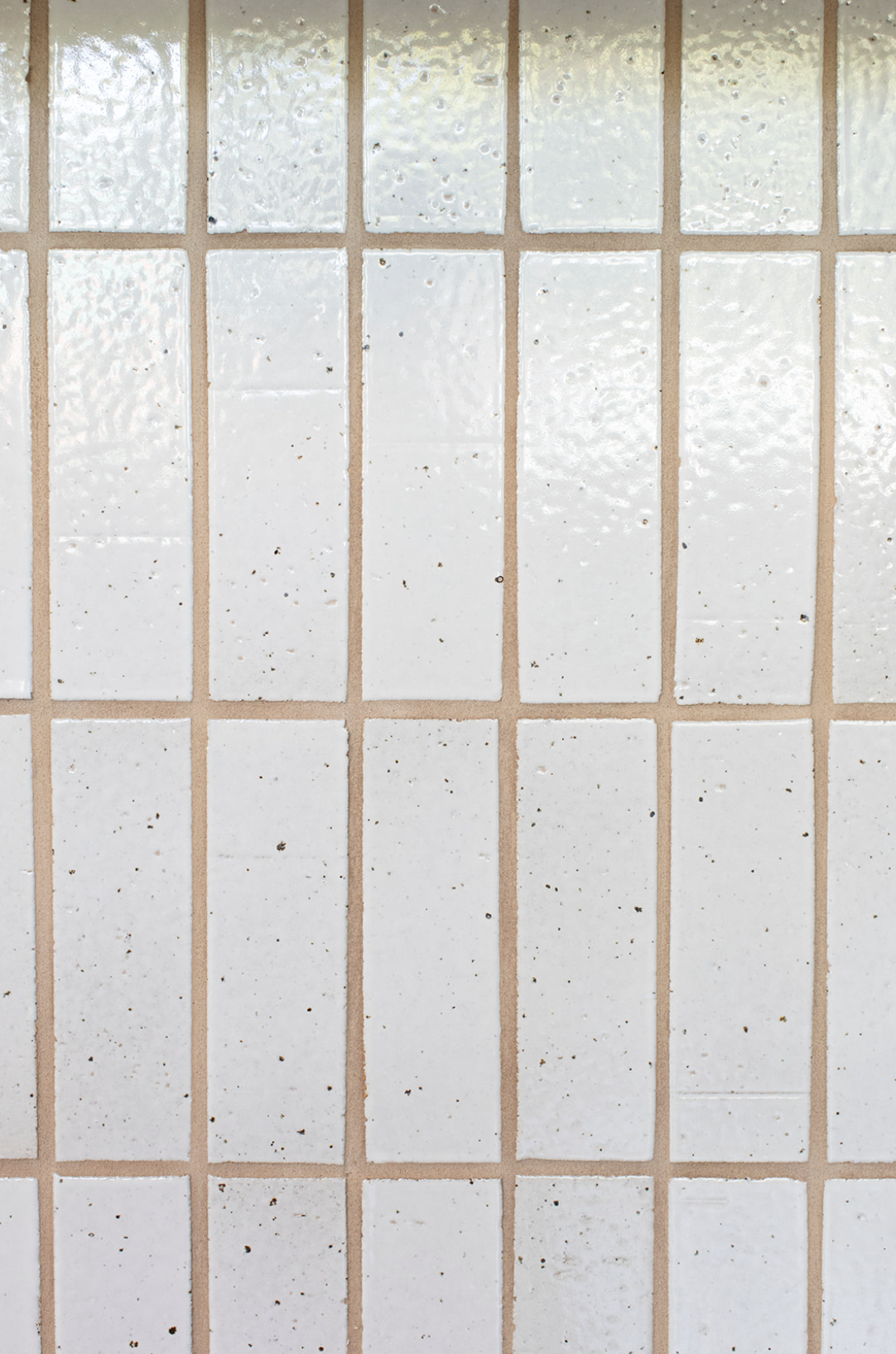 Close-up of a tiled wall with white, textured, square tiles separated by beige grout lines.