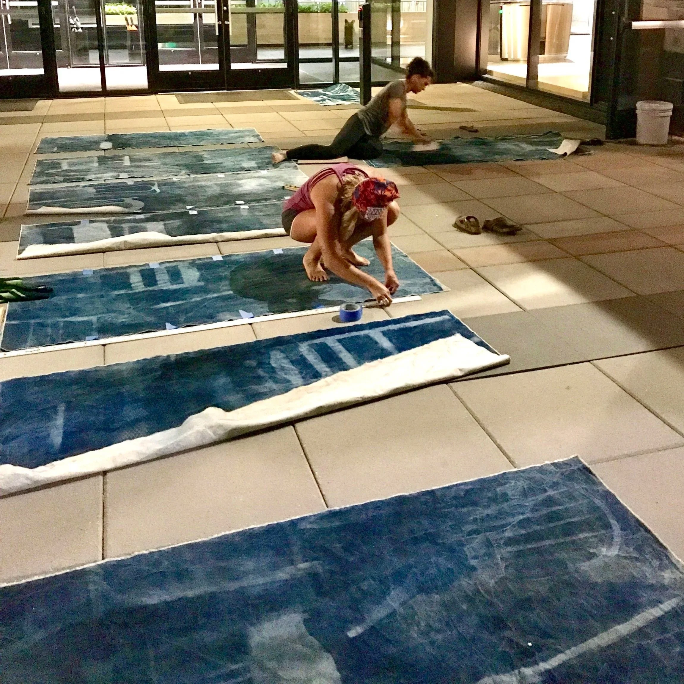 Two young children arranging or working with fabric banners or cloth pieces on the floor outside near glass doors at night.