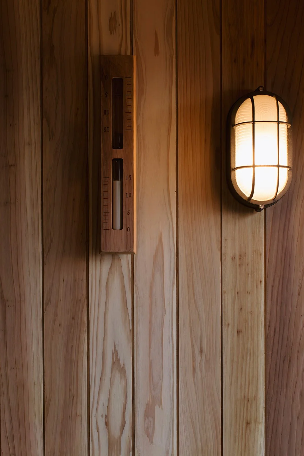 A wooden wall with a thermometer and a wall-mounted light fixture. The thermometer shows about 2 degrees Celsius, and the light emits a warm glow.