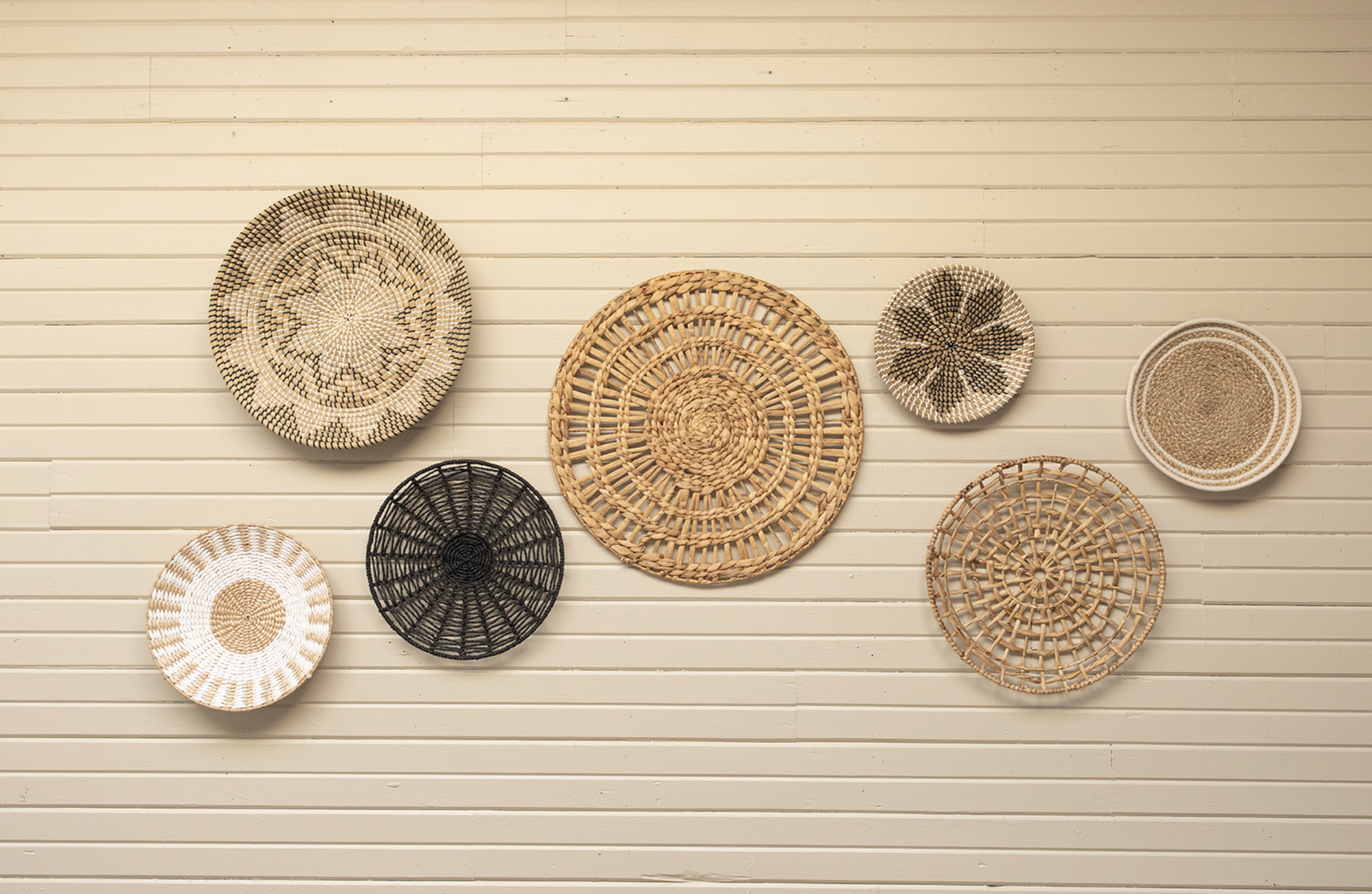 A collection of woven baskets and trays of various sizes and patterns displayed on a white wall.