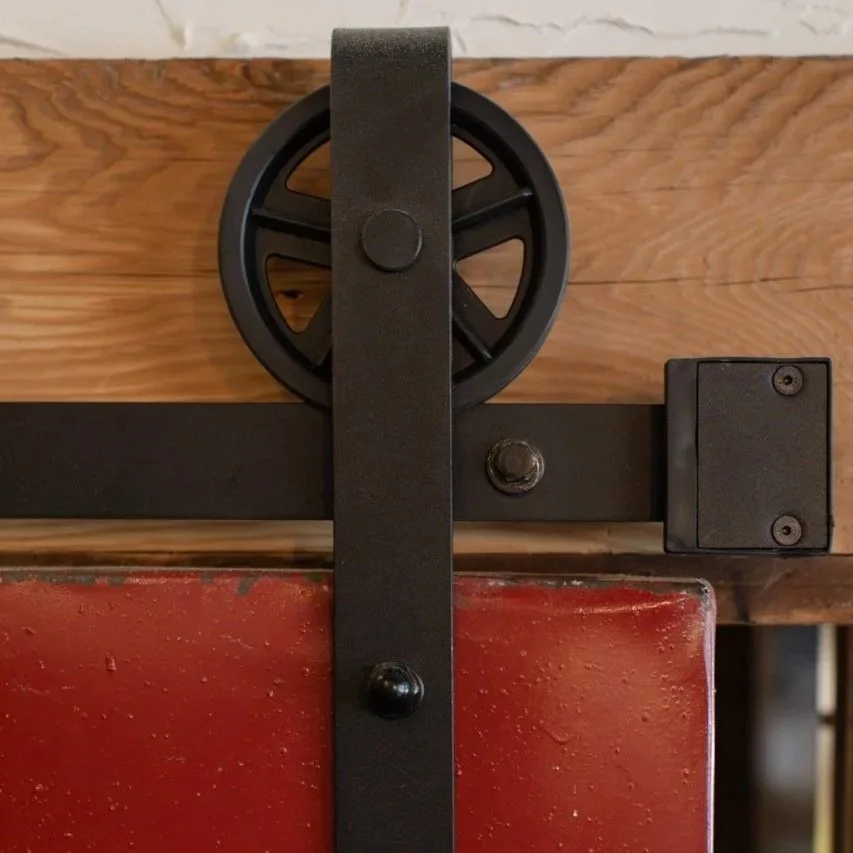 Close-up of a black sliding barn door hardware mechanism mounted on wooden wall and red door panel.