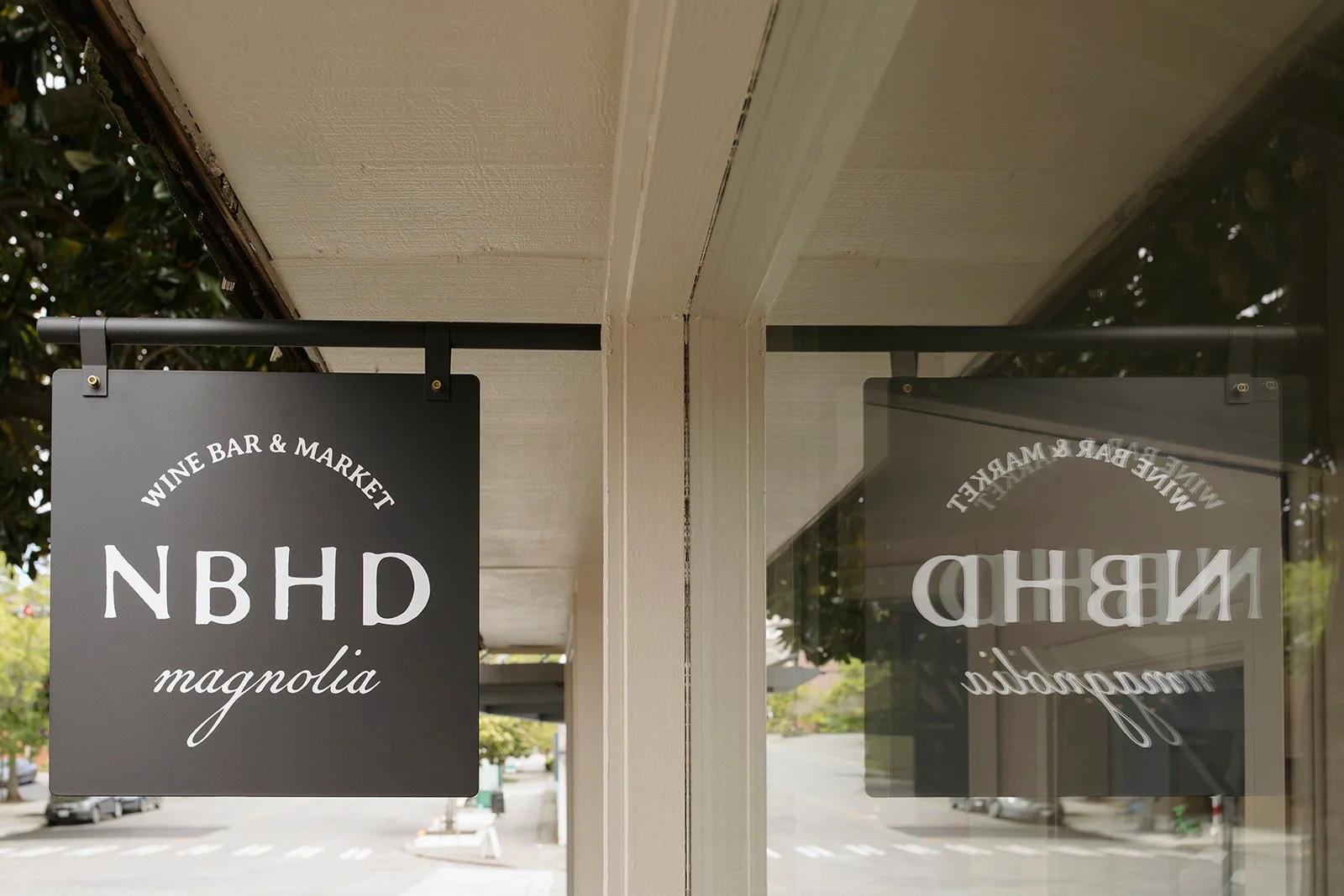 Sign for a wine bar and market named NBHD Magnolia, with the text reflected in a window.