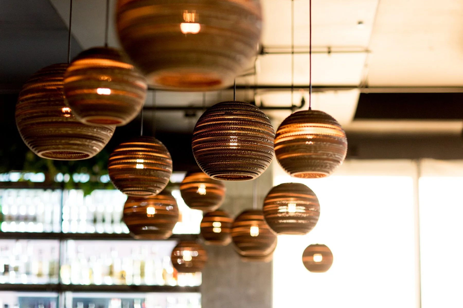 Multiple decorative hanging pendant lights with striped wood or metal patterns, emitting a warm glow in a modern interior space.