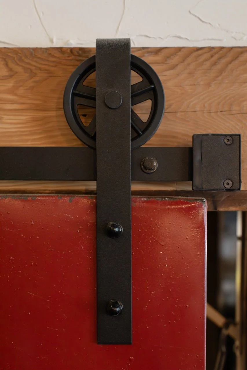 Close-up of a black sliding barn door roller mechanism mounted on a wooden door with black hardware.