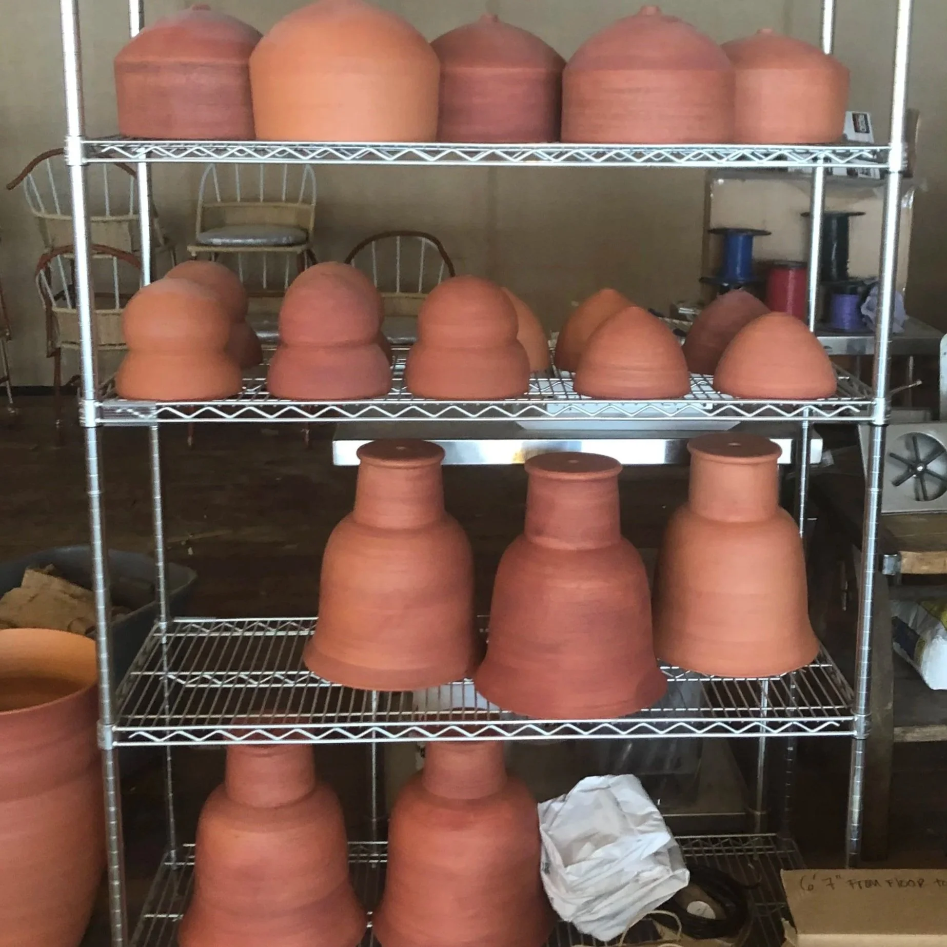Shelves filled with unglazed clay flower pots of various sizes in a workshop or storage room.