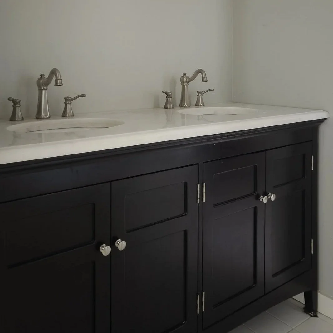 Bathroom vanity with two sinks, silver faucets, and a black cabinet with silver knobs.