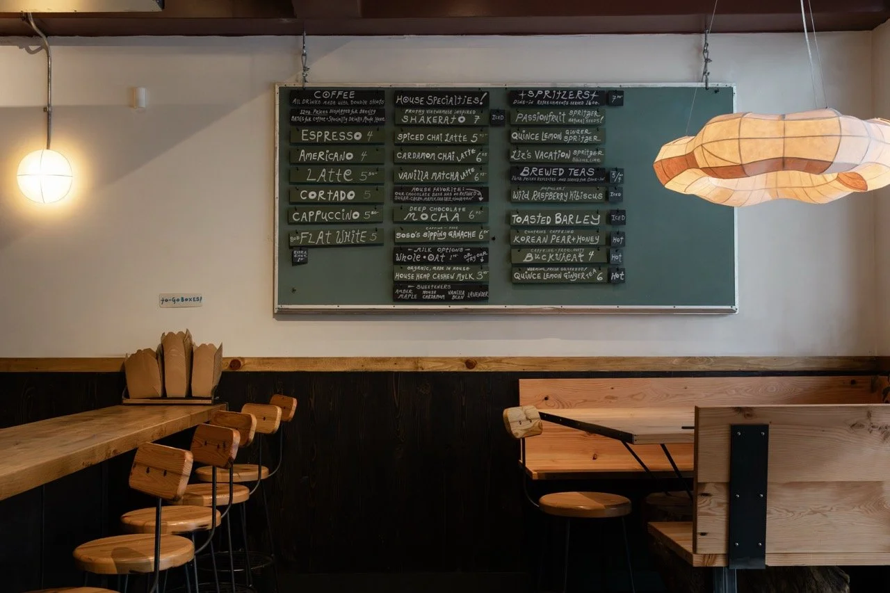 Interior of a café with a chalkboard menu, wooden tables, chairs, and hanging lights.