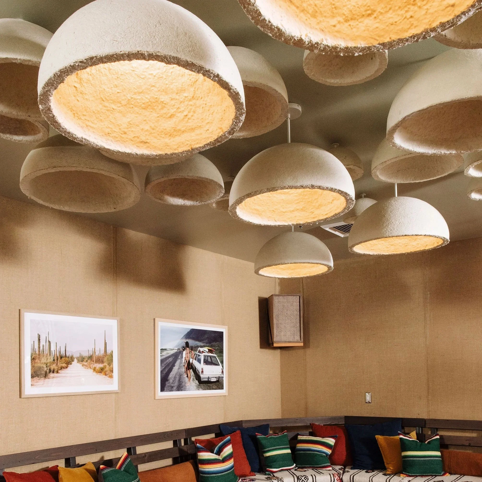Interior of a room with photos on the wall, a wooden bench with colorful striped cushions, and ceiling lights.