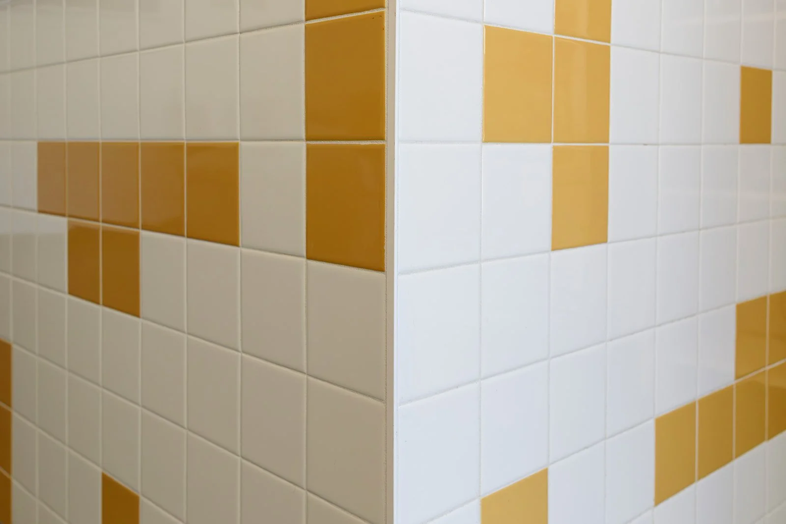 Close-up of tiled wall with alternating white and yellow tiles in a pattern, forming a corner.
