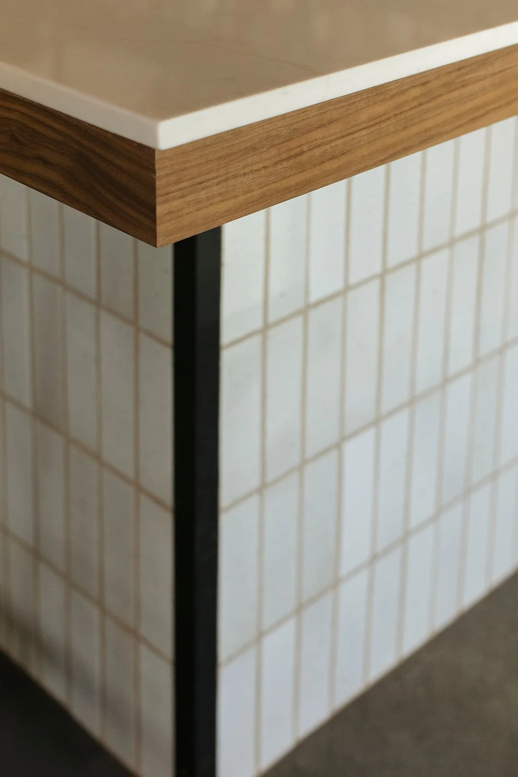 Close-up of a kitchen island with a wooden edge, white countertop, and tiled base with a grid pattern.