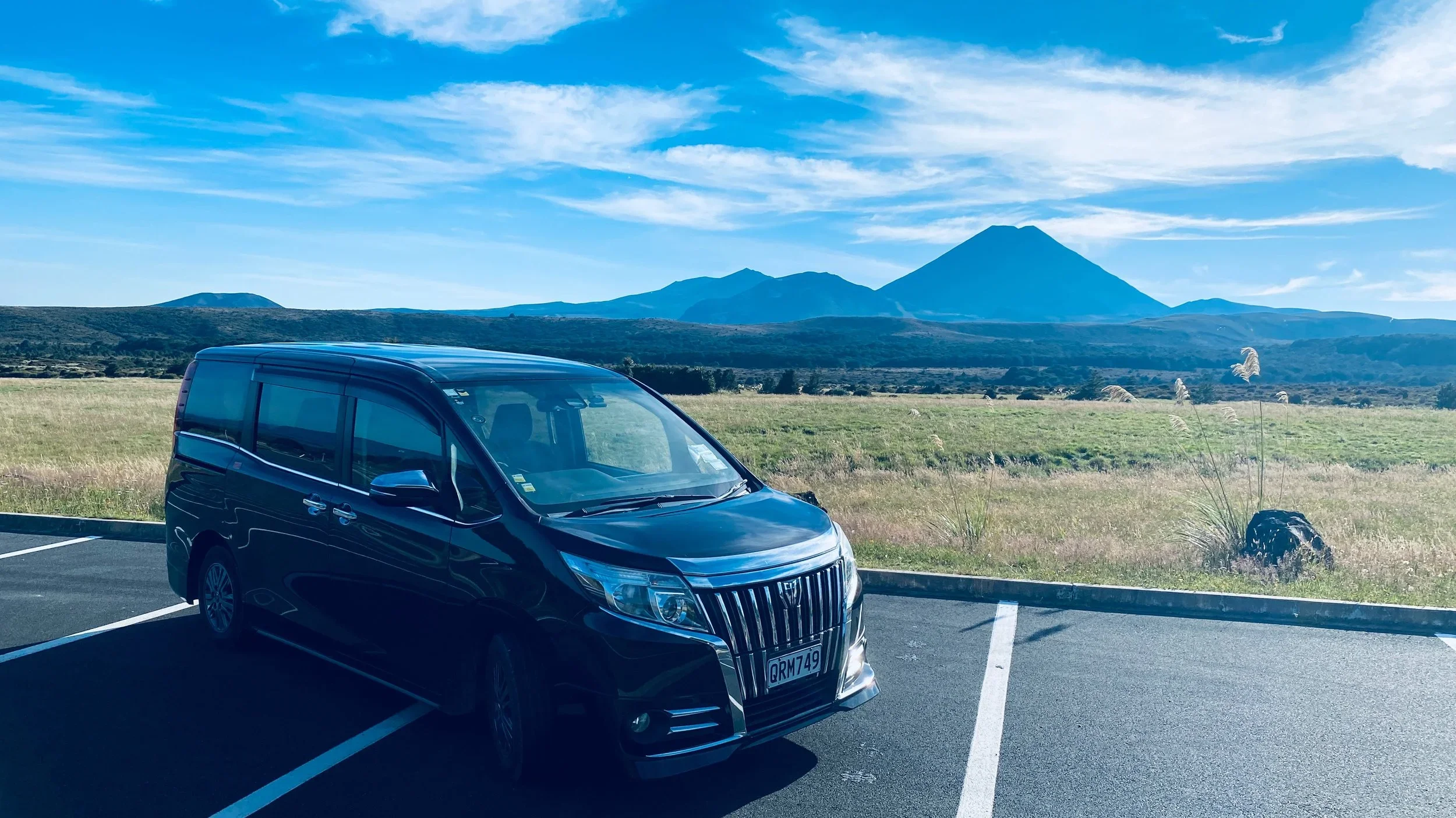 Black minivan parked in a parking lot with a scenic mountainous landscape and blue sky in the background.
