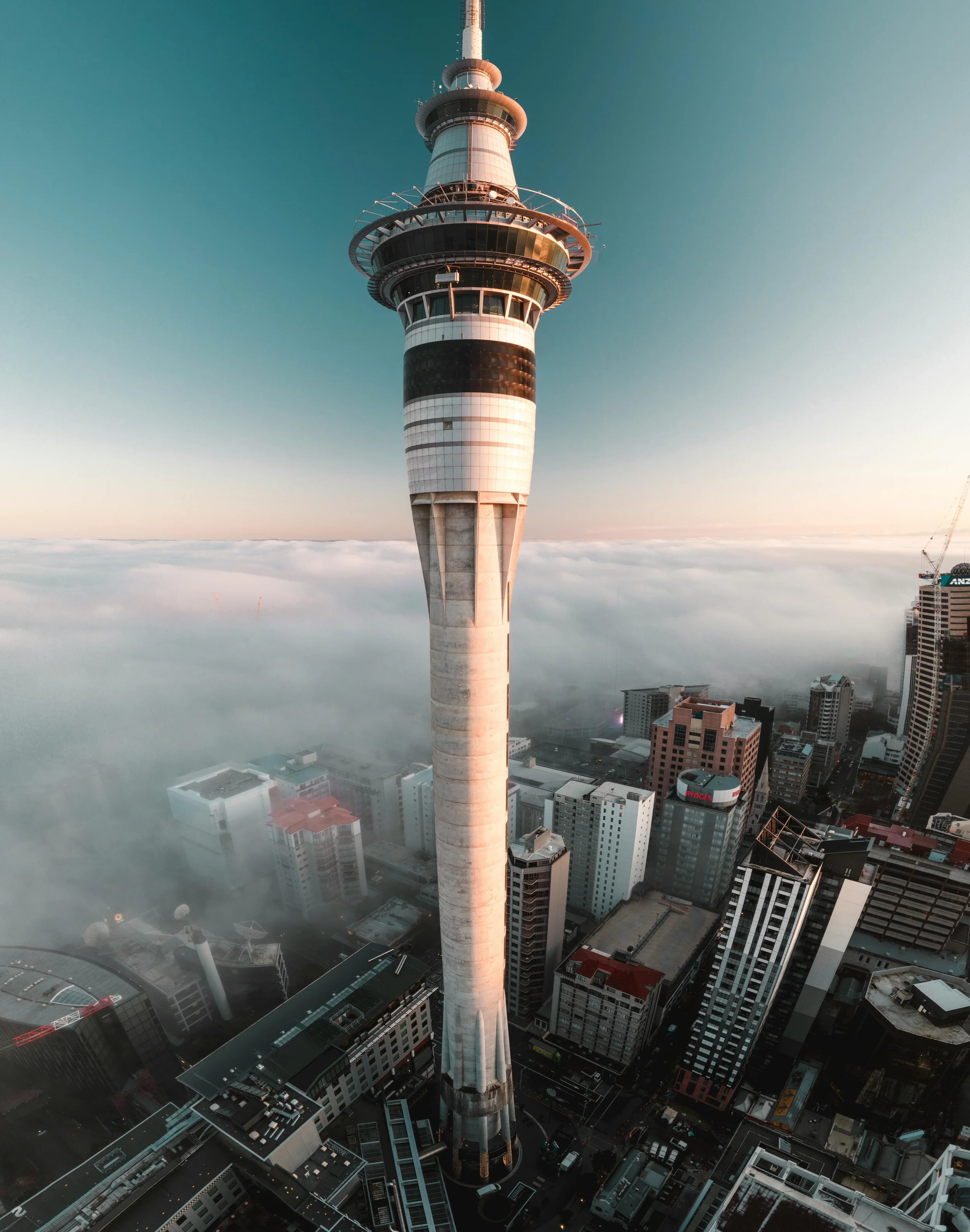 A tall communication tower rises above the city skyline, with a clear sky and some clouds in the background.
