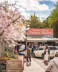 People shopping at Matakana Village Farmers Market with blossoming trees in the background and a sign for Zero Waste Market.