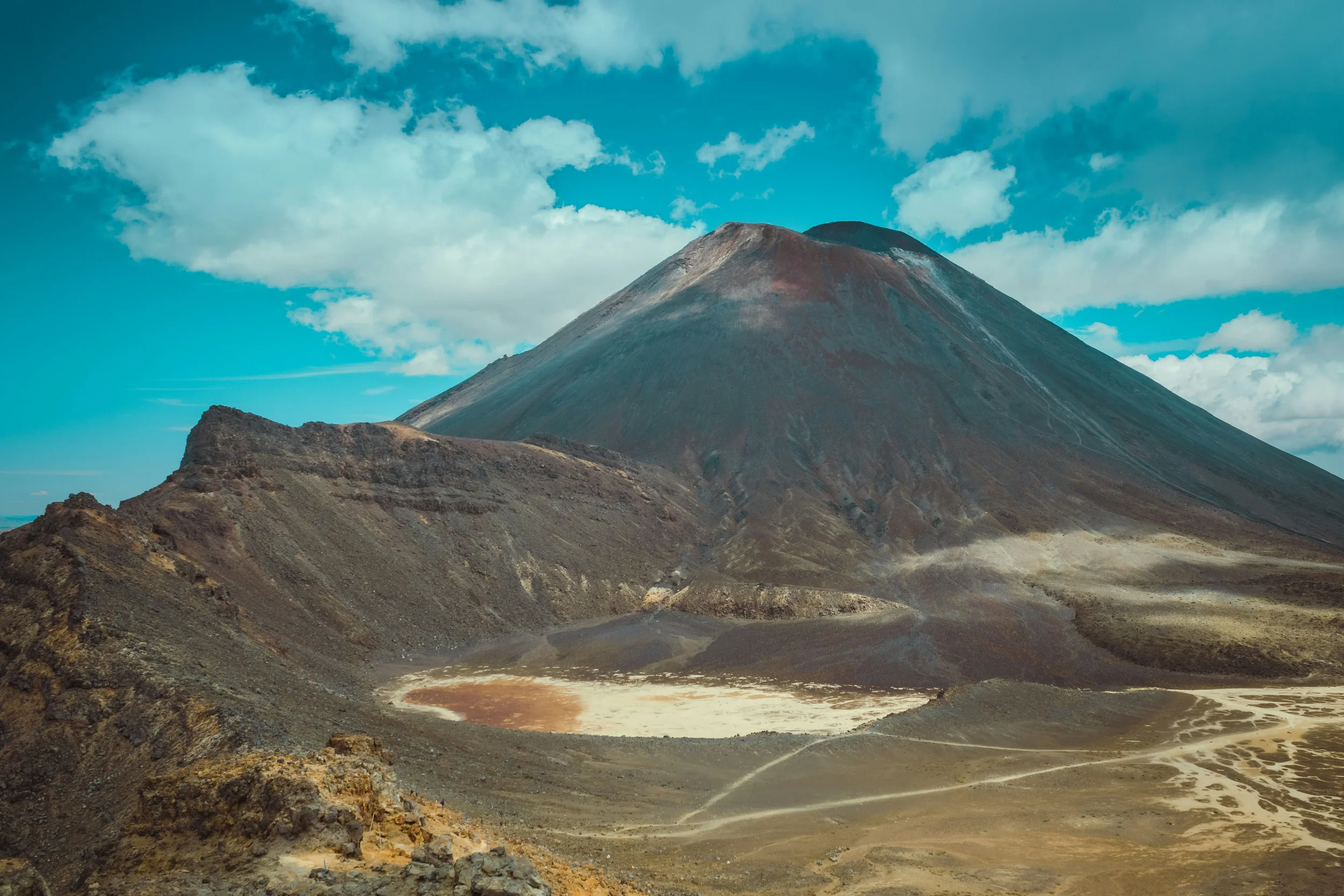 A volcanic mountain with a barren, rocky landscape and a cloudy blue sky.