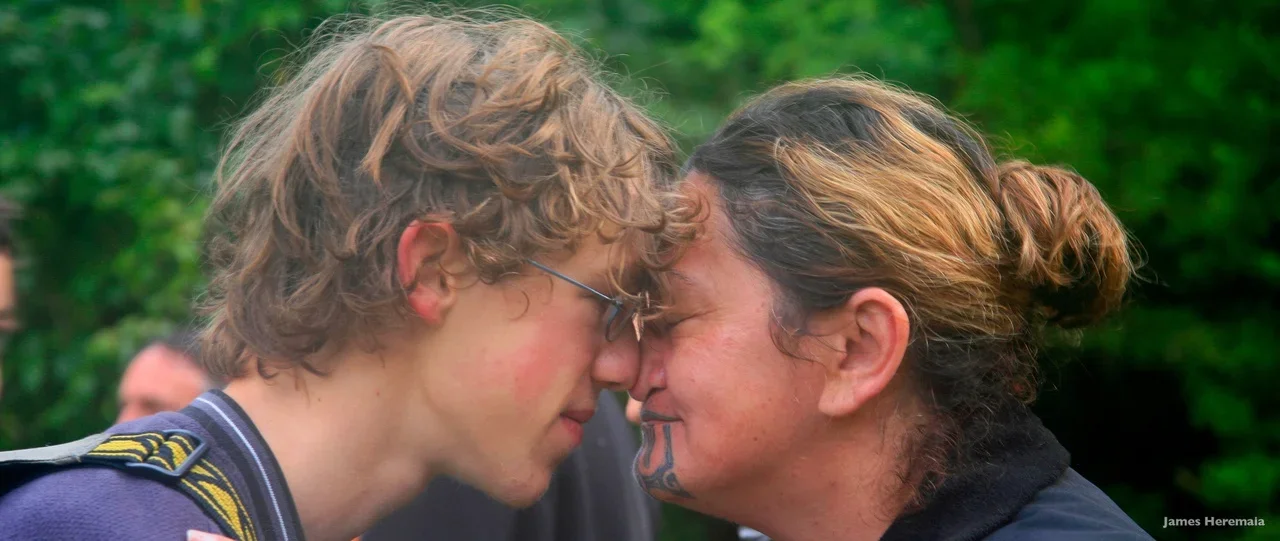 Two people touching foreheads with closed eyes outdoors, with a blurred green background.