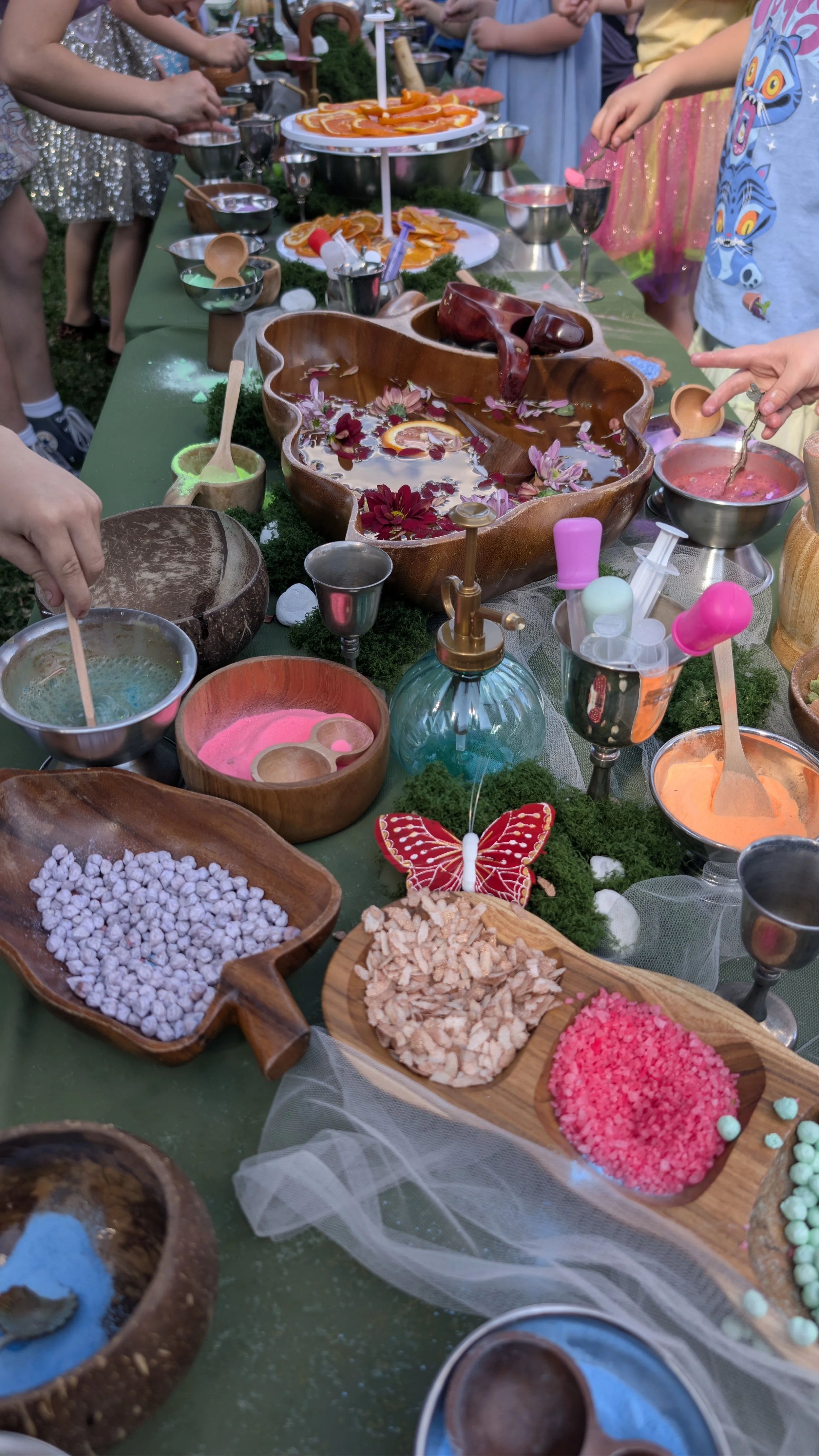 Children are gathered around a table with various colorful potion powder, and decorations for a birthday celebration
