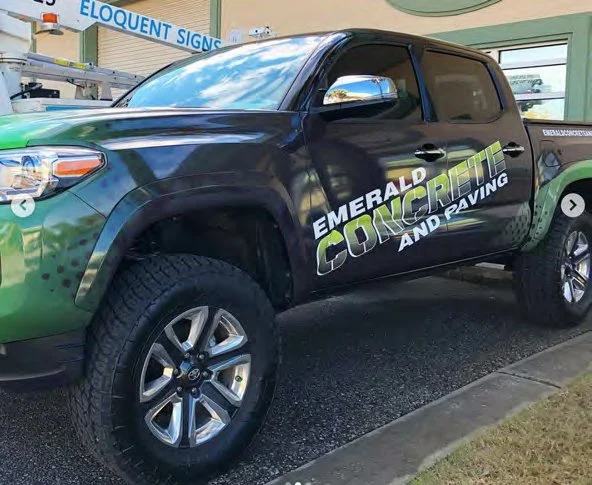 Black pickup truck with branding for Emerald Concrete and Raving, parked outside a building with a sign that reads 'Eloquent Signs'.