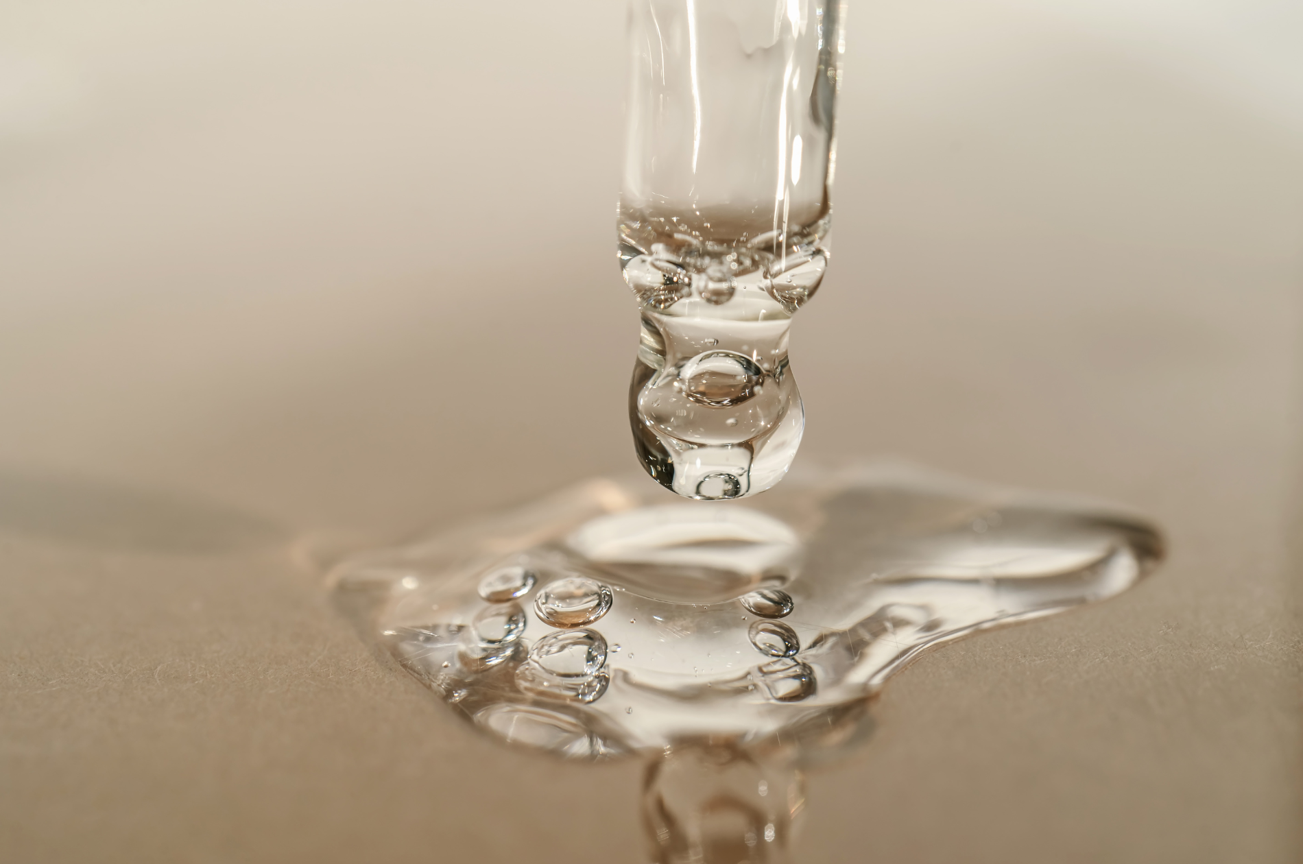 Close-up of a water droplet falling into a puddle, creating bubbles and ripples on a smooth surface.