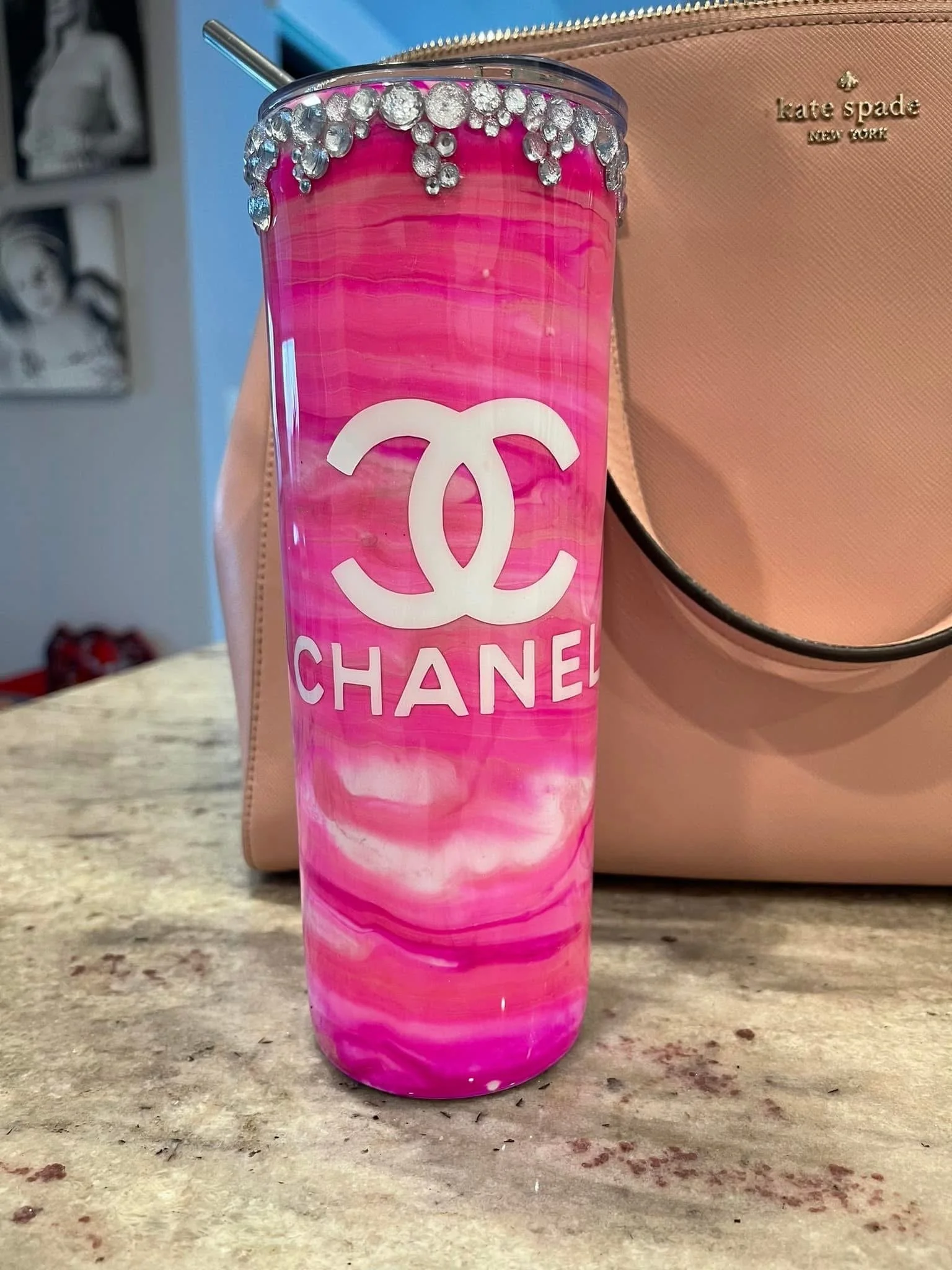 Pink Marbled Chanel tumbler with rhinestone embellishments on the rim, placed on a beige countertop with a blush-colored Kate Spade purse nearby.