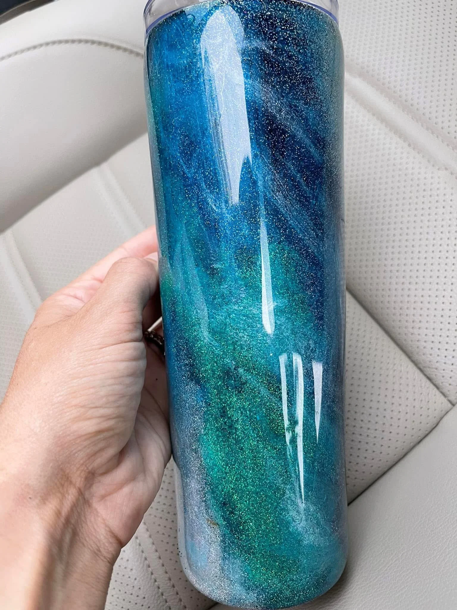 A clear plastic tumbler with a blue and green galaxy design, featuring a white rocket and small white stars, held by a person's hand.