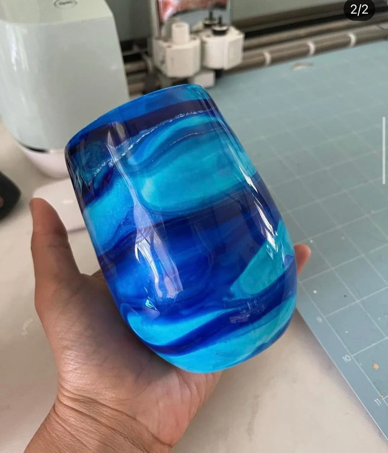 Close-up of a hand holding a blue and turquoise marble-patterned glass vase.