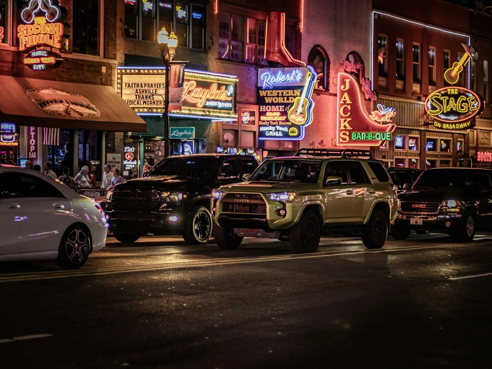Lower Broadway in Nashville at night with neon honky-tonk signs, where mobile surveillance follows the night