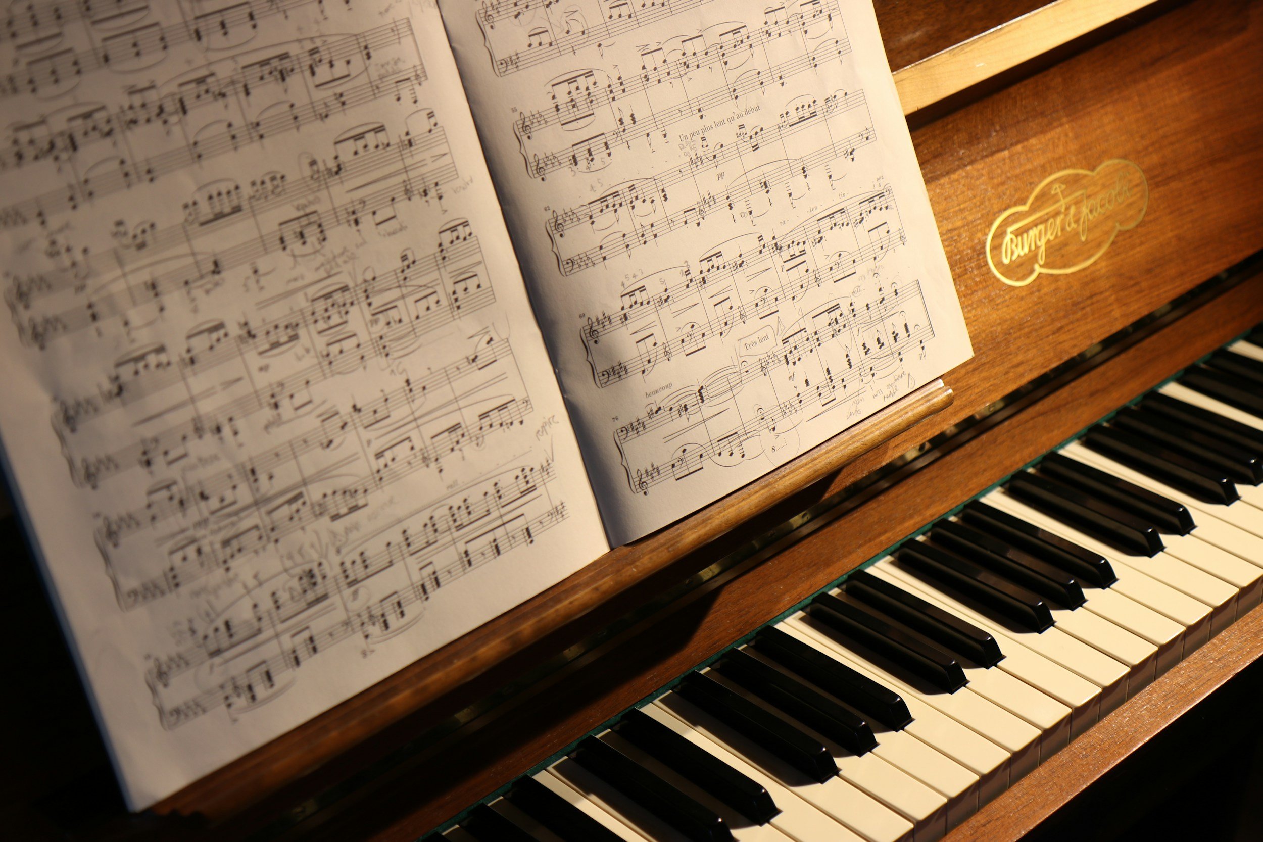 Open sheet music on a wooden piano. The sheet music contains musical notations and handwritten notes. Part of the piano keys are visible underneath the sheet music.