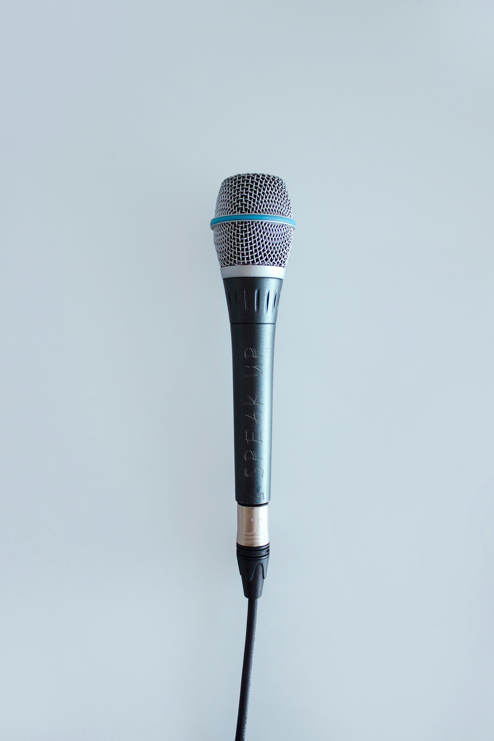 A close-up of a handheld microphone against a plain light blue background.