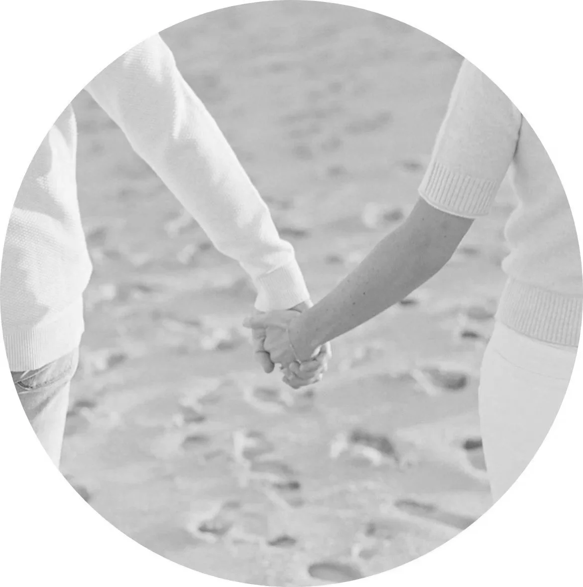 Two people holding hands while walking on a sandy beach