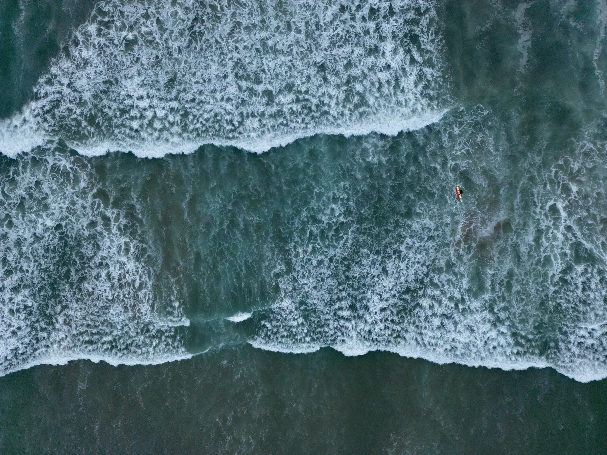 Aerial view of ocean waves and a small boat near the shoreline.