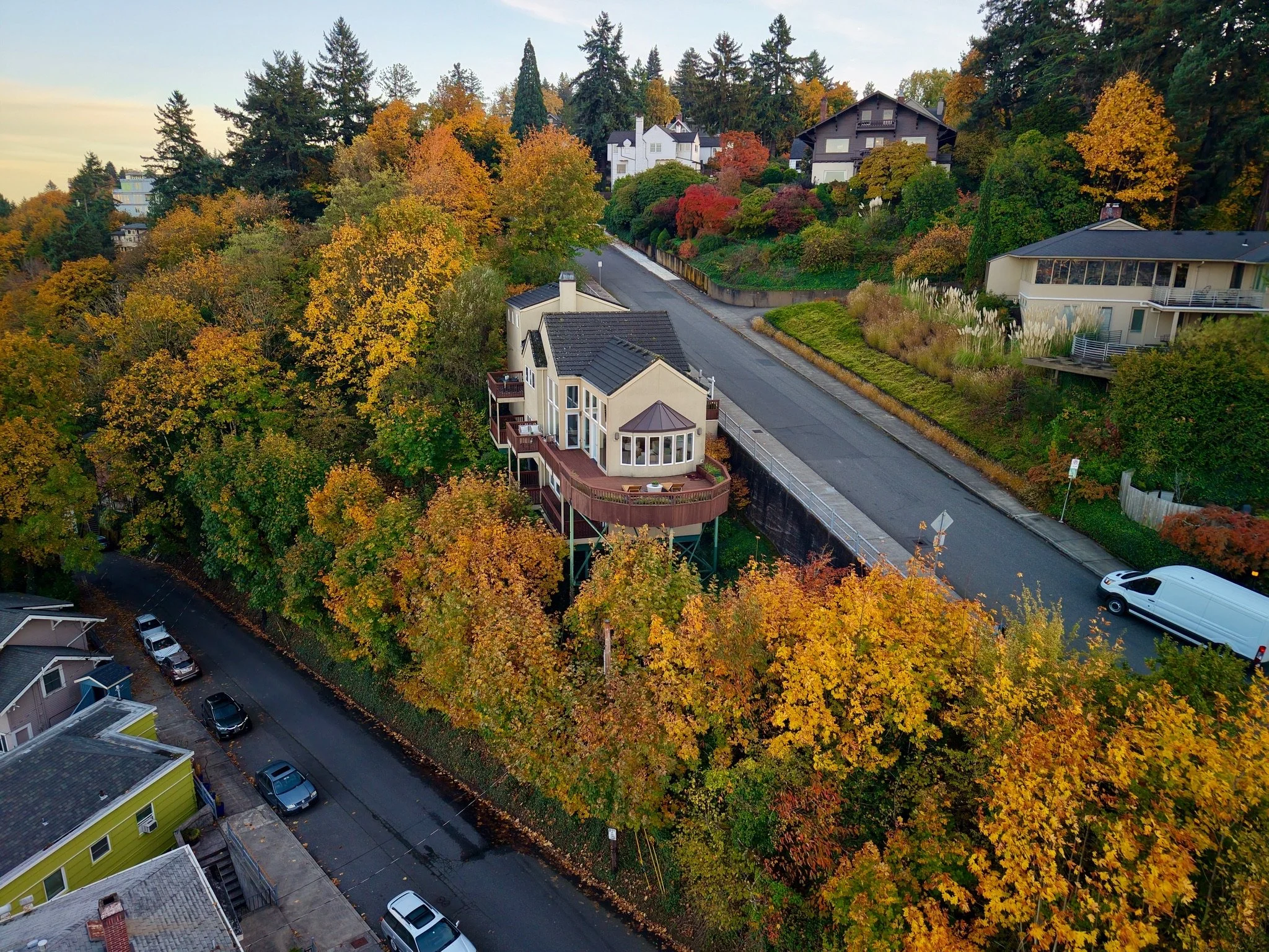 An aerial view of a residential neighborhood during fall, showcasing colorful autumn trees, houses, and a street with parked cars.