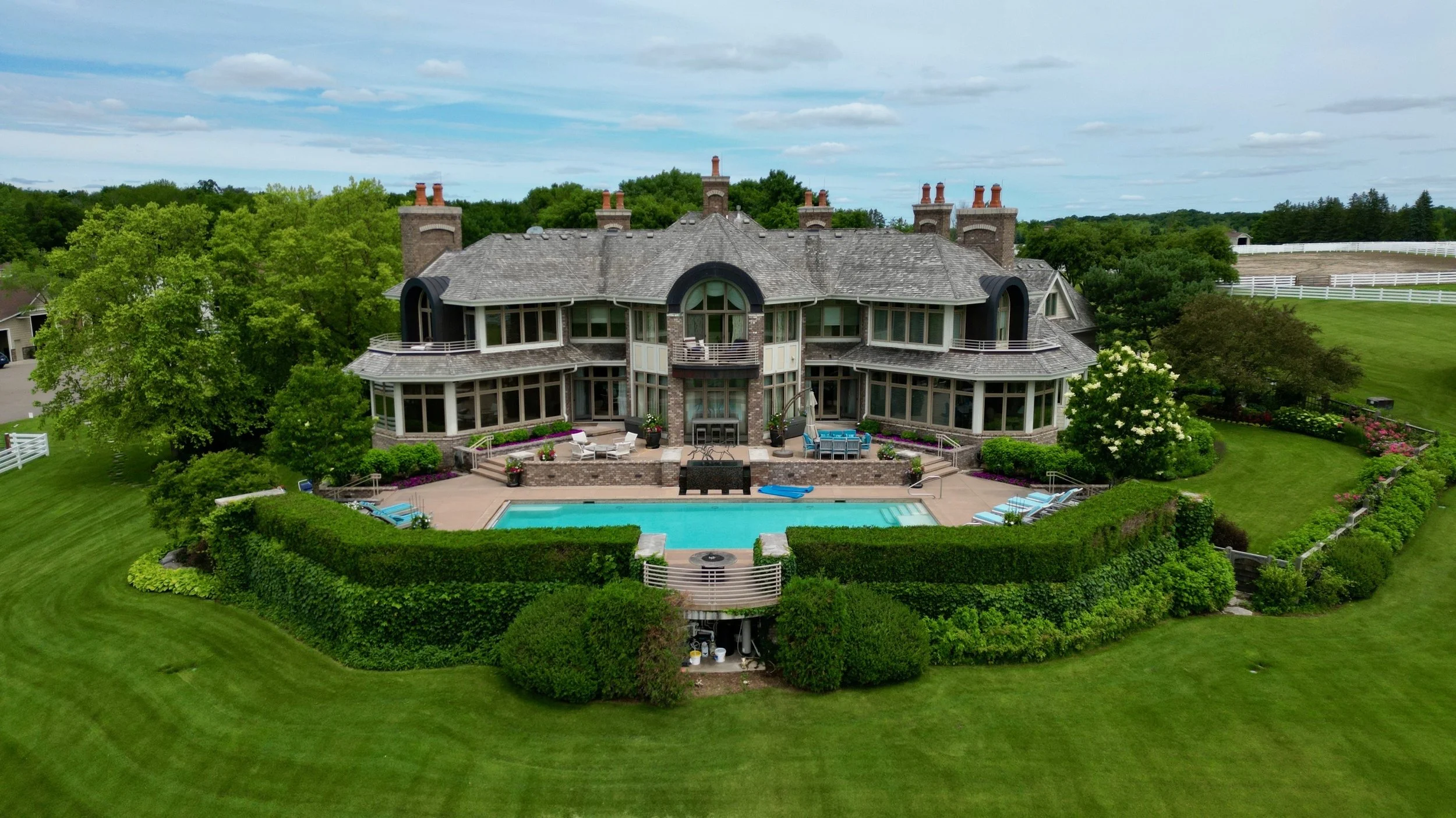 A large, elegant house with a pool in the backyard, surrounded by well-maintained green lawns, trees, and landscaped gardens.