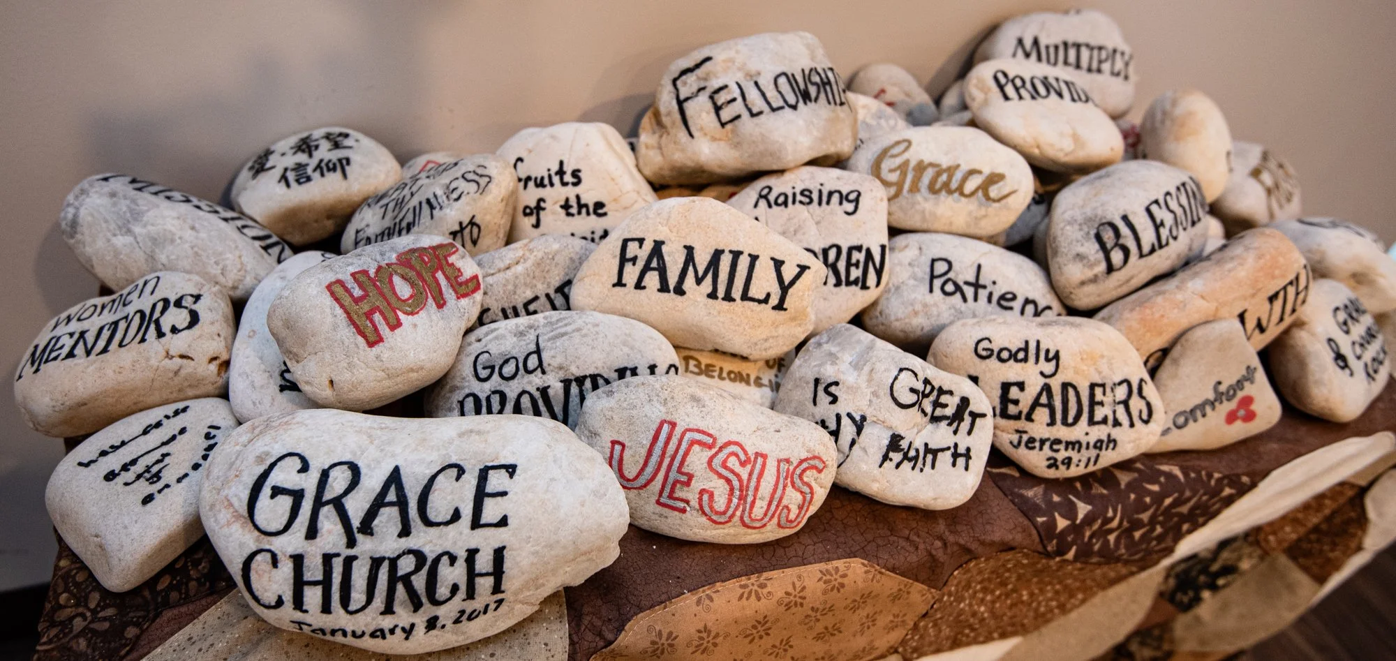A collection of painted stones with various words and phrases, including 'HOPE,' 'FAMILY,' 'GRACE,' and 'JESUS,' arranged on a surface.